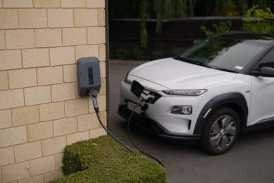 White electric car plugged into charging point on house