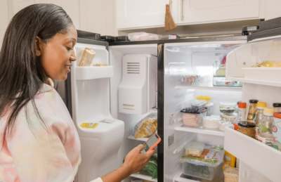 Woman looking at phone with doors open on wide American style fridge freezer