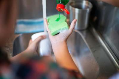 Person holding washing up sponge and cup with detergent on sponge 