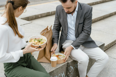 Woman and man sitting on steps outside with takeaway cartons of food