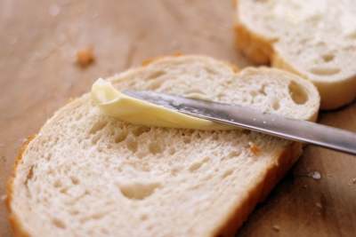 Butter or margarine being spread on piece of white bread