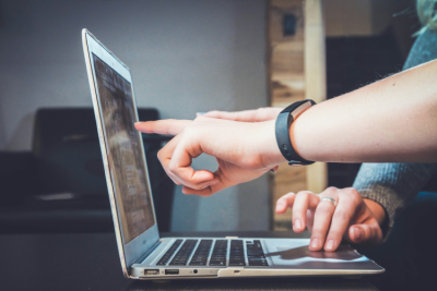 Laptop with hands from two people pointing at the screen