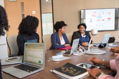 Group of Black women sitting around a boardroom table with laptops and documents