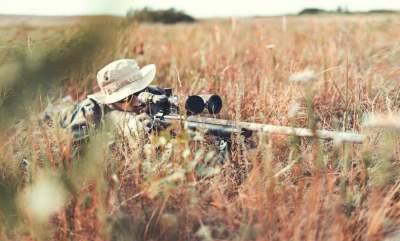 Person hiding in vegetation with shooting equipment and binoculars