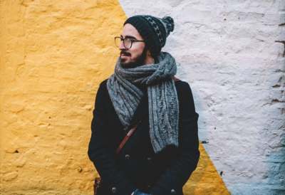 Man wearing hat, coat and scarf standing against yellow and white wall