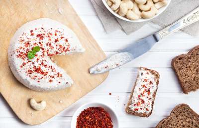 Aerial view of round soft vegan cheese, with bowl of cashews, and small pieces of bread