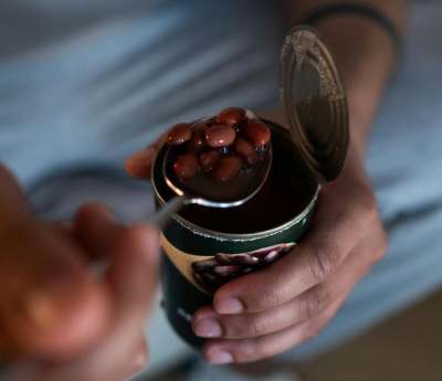 Person holding open tin can of beans and holding a spoon with beans on