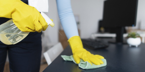 Person wearing yellow rubber gloves cleaning desk with spray liquid