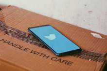 Mobile phone with blue Twitter symbol, lying on top of cardboard box which reads 'handle with care'