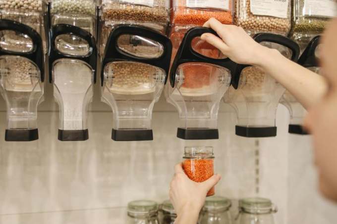 Person using bulk refill unit to fill jar with red lentils