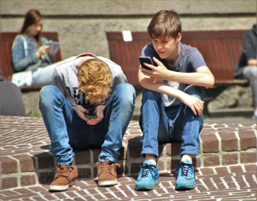 Two teenage boys looking at mobile phones, sat down outside