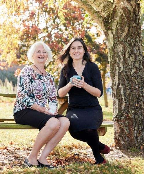 Two women sitting on bench with tree behind